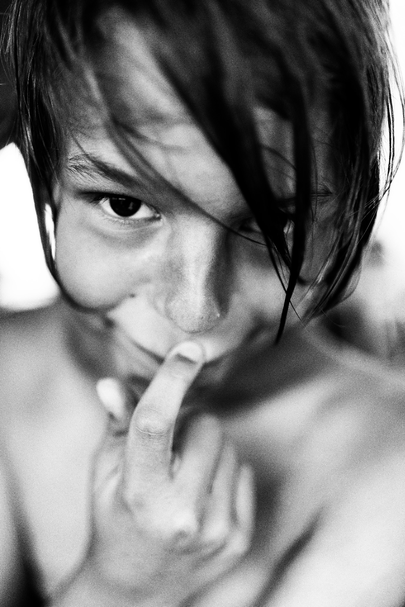 Czarno-biały portret chłopca z mokrymi włosami, zakrywającego usta palcem, z wyrazem tajemniczości w oczach.