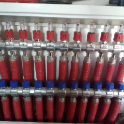 Rozdzielacz ogrzewania podłogowego z jedenastoma obiegami, z czerwonymi rurami i przepływomierzami z czerwonymi elementami, numery od 1 do 11.