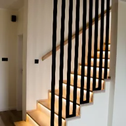 Nowoczesne schody z podświetleniem LED pod stopniami i czarną, pionową balustradą, widok z dołu.