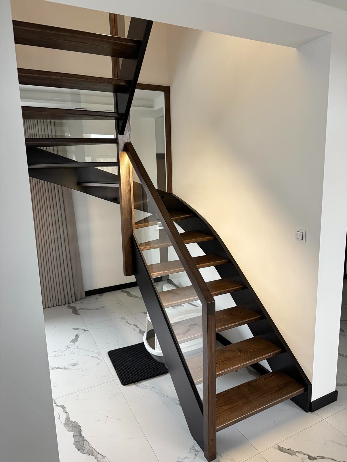 Nowoczesne schody drewniane z czarną konstrukcją i szklaną balustradą, widok z dołu, marmurowa podłoga, minimalistyczny design.