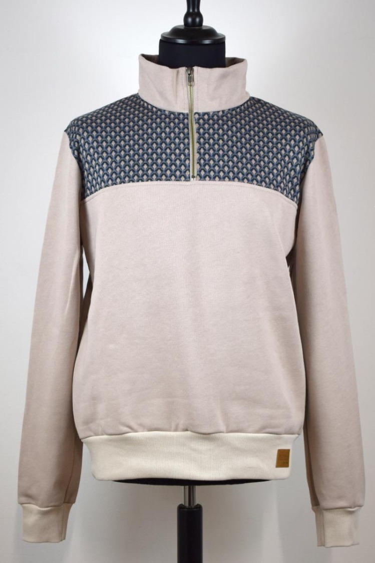 Beżowa bluza z krótkim suwakiem i geometrycznym wzorem na ramionach, prezentowana na manekinie na jasnym tle.