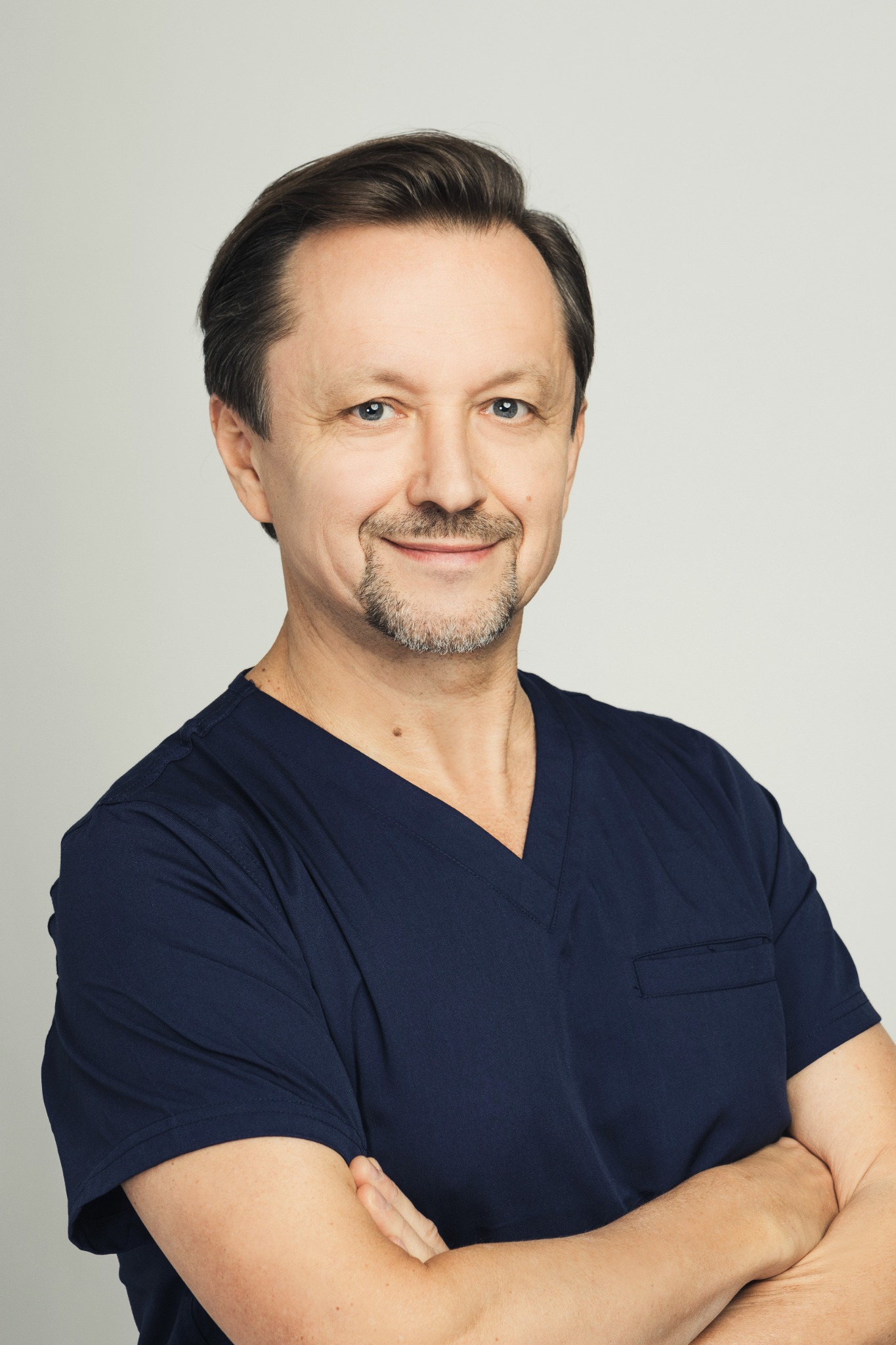 Portret uśmiechniętego technika dentystycznego w granatowym uniformie, z rękami skrzyżowanymi na piersi, na neutralnym tle.