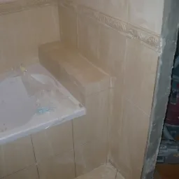 Płytki ceramiczne w łazience w trakcie remontu, widoczna wanna zabezpieczona folią, fragment ściany z ornamentem i odkurzacz przemysłowy Kress w tle.