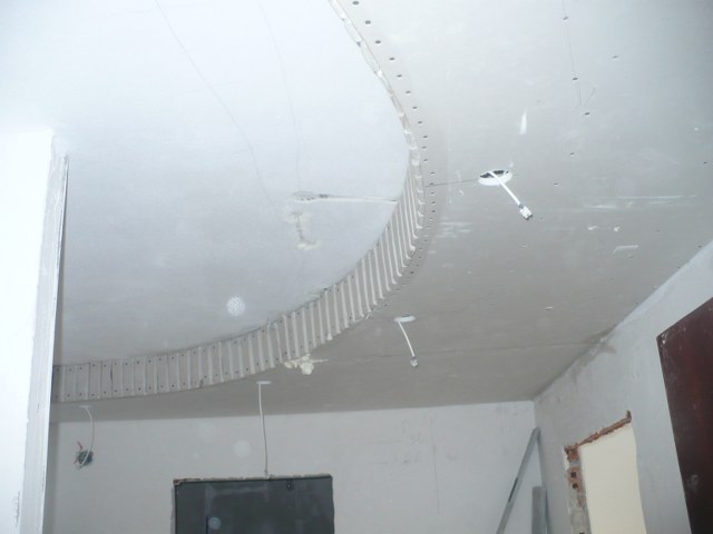 Przygotowanie do montażu sufitu podwieszanego: widoczne profile montażowe na suficie, kable oświetleniowe wystające z otworów, surowy stan wykończenia wnętrza.