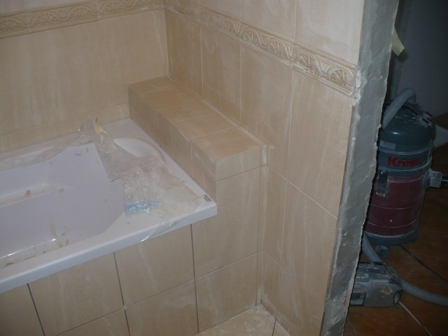 Płytki ceramiczne w łazience w trakcie remontu, widoczna wanna zabezpieczona folią, fragment ściany z ornamentem i odkurzacz przemysłowy Kress w tle.