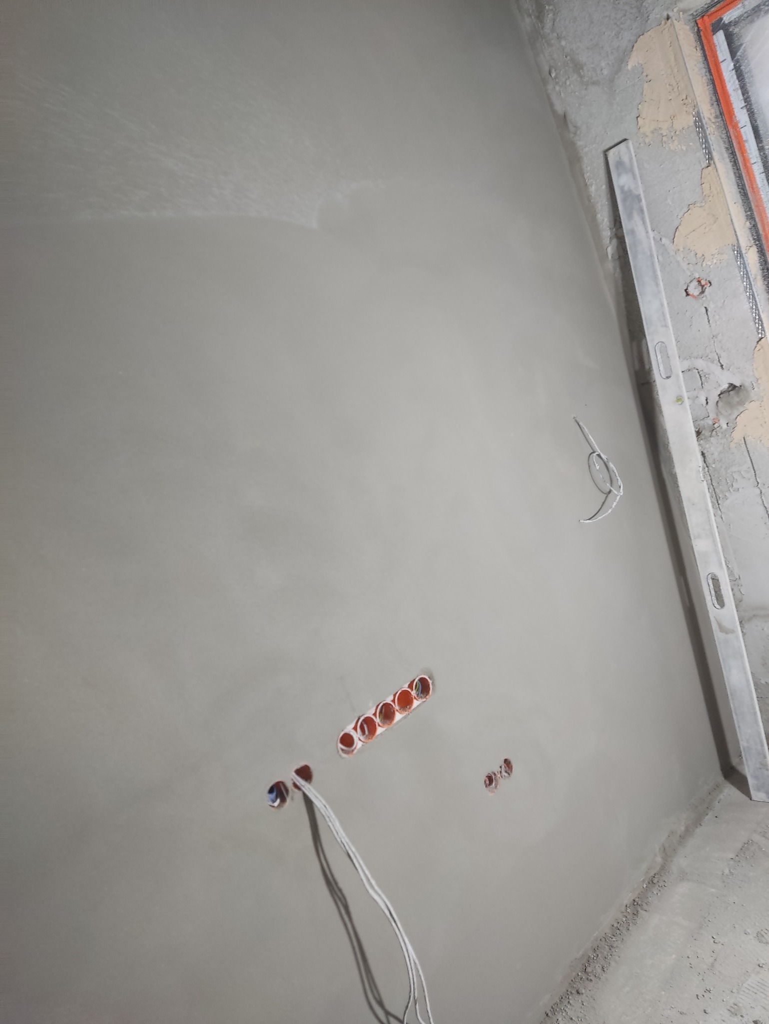 Świeżo położony tynk na ścianie z puszkami elektrycznymi w Rutka-Tartak. Widoczna poziomica i wystające przewody. Gładka powierzchnia gotowa do dalszych prac.