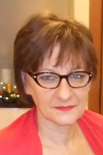 Portret kobiety w okularach i czerwonej bluzce, z małym stroikiem świątecznym w tle.