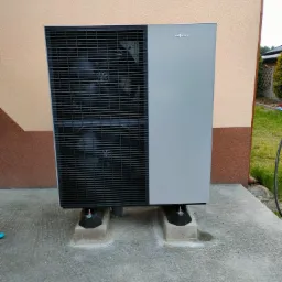 Zewnętrzna jednostka pompy ciepła Viessmann, zamontowana na betonowym fundamencie z użyciem antywibracyjnych podkładek, na tle elewacji budynku.