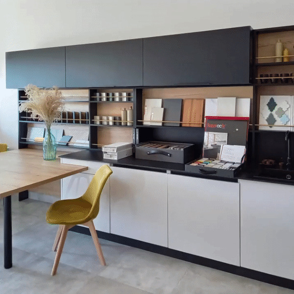 Prezentacja materiałów wykończeniowych w showroomie w Krakowie: próbki płytek, paneli i farb ułożone na blacie kuchennym z żółtym krzesłem w tle, sugerujące proces projektowania wnętrza.