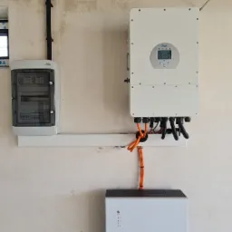 Instalacja magazynu energii Enovance z inwerterem Deye na ścianie o nierównej fakturze. Widoczne przewody, skrzynka elektryczna. Realizacja wewnątrz budynku.