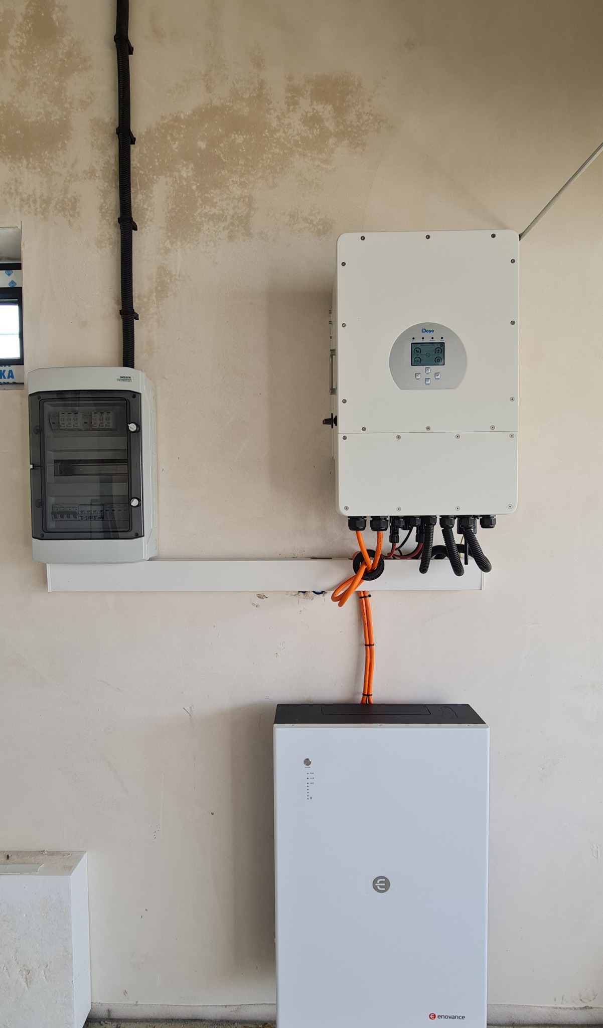 Instalacja magazynu energii Enovance z inwerterem Deye na ścianie o nierównej fakturze. Widoczne przewody, skrzynka elektryczna. Realizacja wewnątrz budynku.