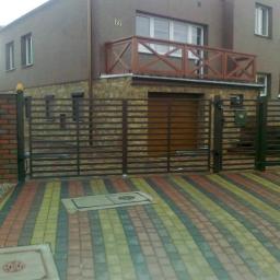 PPUH Aplauz - Nowoczesna posesja z automatyczną bramą wjazdową z poziomych profili, kolorowa kostka brukowa na podjeździe, budynek z balkonem w tle.