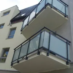 Elewacja budynku z dwoma balkonami z czarnymi balustradami i matowym szkłem, widok z dołu.