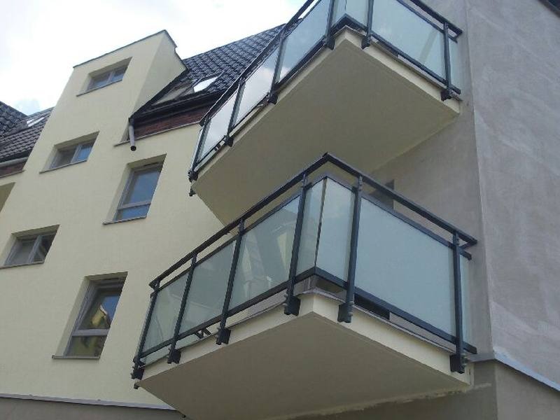 Elewacja budynku z dwoma balkonami z czarnymi balustradami i matowym szkłem, widok z dołu.