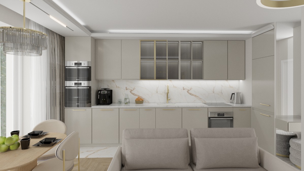 Elegancka, beżowa kuchnia z marmurowym blatem i złotymi akcentami, oświetlona wiszącą lampą. Widoczny stół z owocami i część sofy.