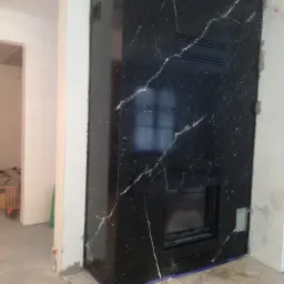 Obudowa kominka z czarnego kamienia z białymi żyłami, w trakcie montażu, widoczne niedoskonałości wykończenia ściany.