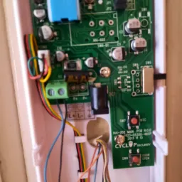 Otwarta obudowa wideodomofonu z widoczną elektroniką, płytką PCB z elementami i podłączonymi kablami, przyciski otwierania drzwi i logo Cyclop Security.