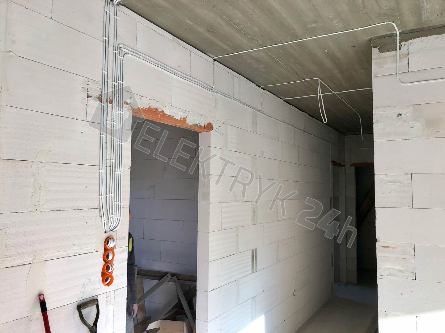 Surowy stan: białe ściany z betonu komórkowego, widoczne kable elektryczne prowadzone w peszlach i puszkach, sufit betonowy, wnętrze w trakcie prac elektrycznych.