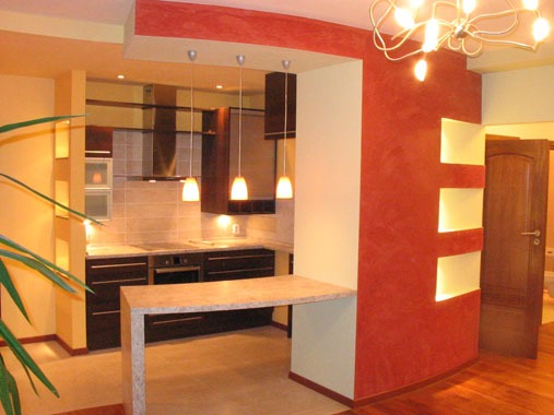 Nowoczesna kuchnia z barkiem w Warszawie, ściana z dekoracyjną fakturą w odcieniach czerwieni i wnękami oświetleniowymi, drewniana podłoga i wiszące lampy nad blatem.