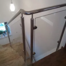 Szklana balustrada z nierdzewnymi słupkami i poręczą, zamocowana na schodach wyłożonych płytkami imitującymi marmur, widok z góry.