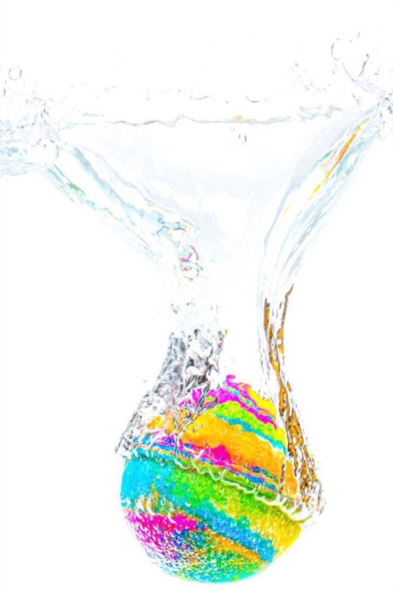 Kolorowa kula zanurzona w wodzie, tworząca efektowne rozpryski i wiry na białym tle.