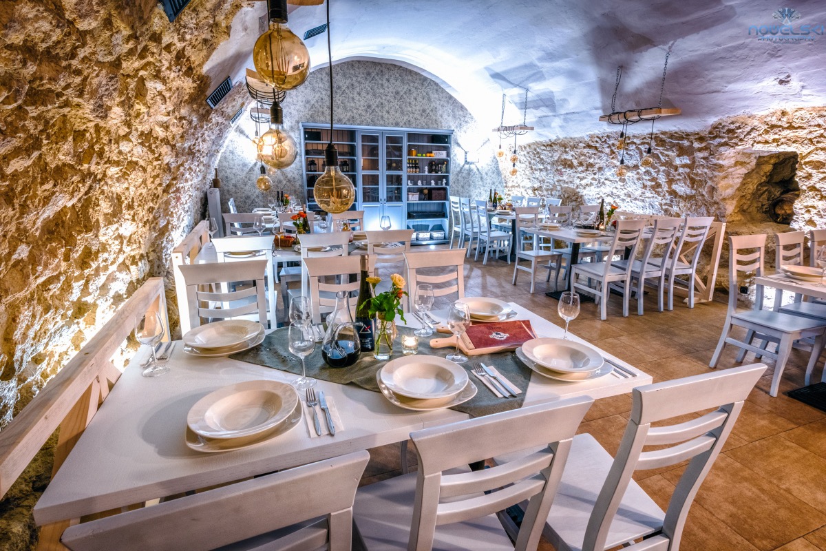 Ustawione stoły z białymi krzesłami i zastawą w restauracji o kamiennych ścianach i oświetleniu w stylu retro.