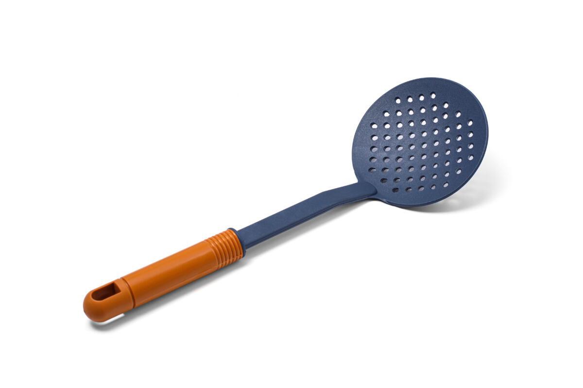 Niebieska łyżka cedzakowa z pomarańczową rączką, leżąca ukośnie na białym tle, z wyraźnym cieniem.