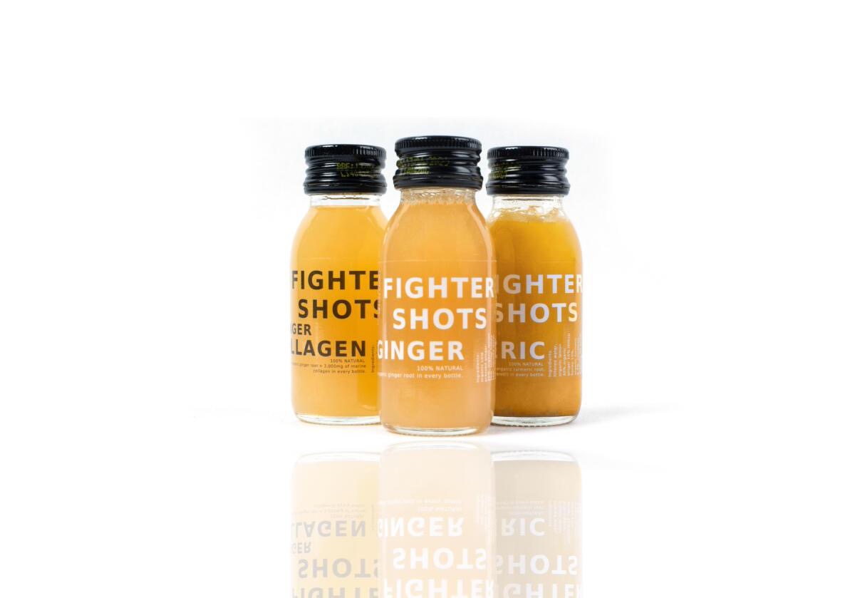 Trzy butelki napojów funkcjonalnych Fighter Shots: Collagen, Ginger i Turmeric, ustawione na białym tle z odbiciem.