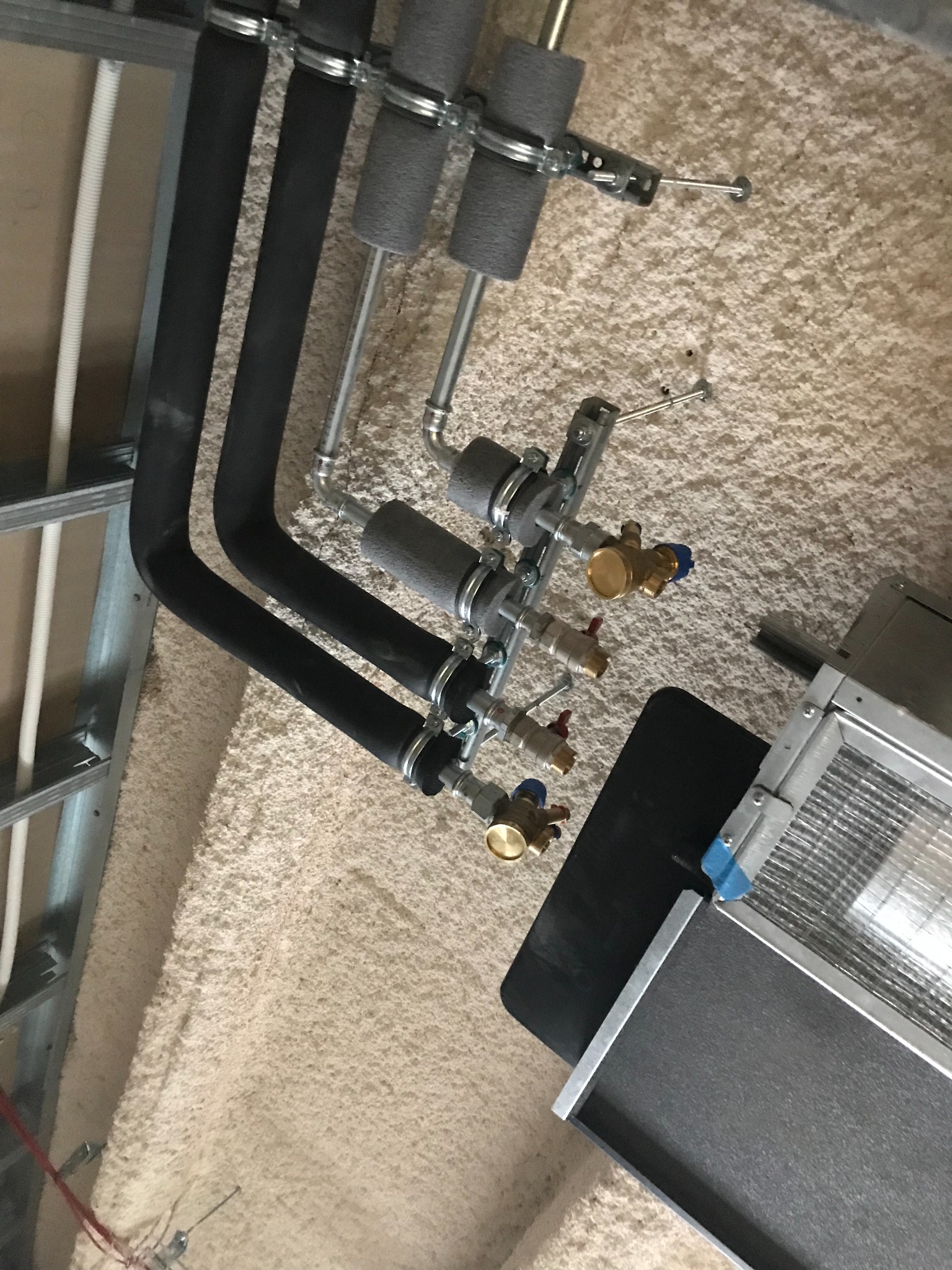 Izolowane czarne rury instalacji grzewczej z zaworami, zamocowane do ściany pokrytej pianą izolacyjną, widok z góry.