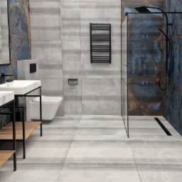Nowoczesna łazienka z szarymi płytkami imitującymi beton, akcentami w kolorze miedzi i niebieskiego, czarną armaturą, kabiną prysznicową typu walk-in i podwieszaną miską WC.