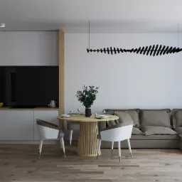 Jasne wnętrze salonu z aneksem kuchennym: drewniana podłoga, okrągły stół z kwiatami, szara sofa i designerska lampa sufitowa.