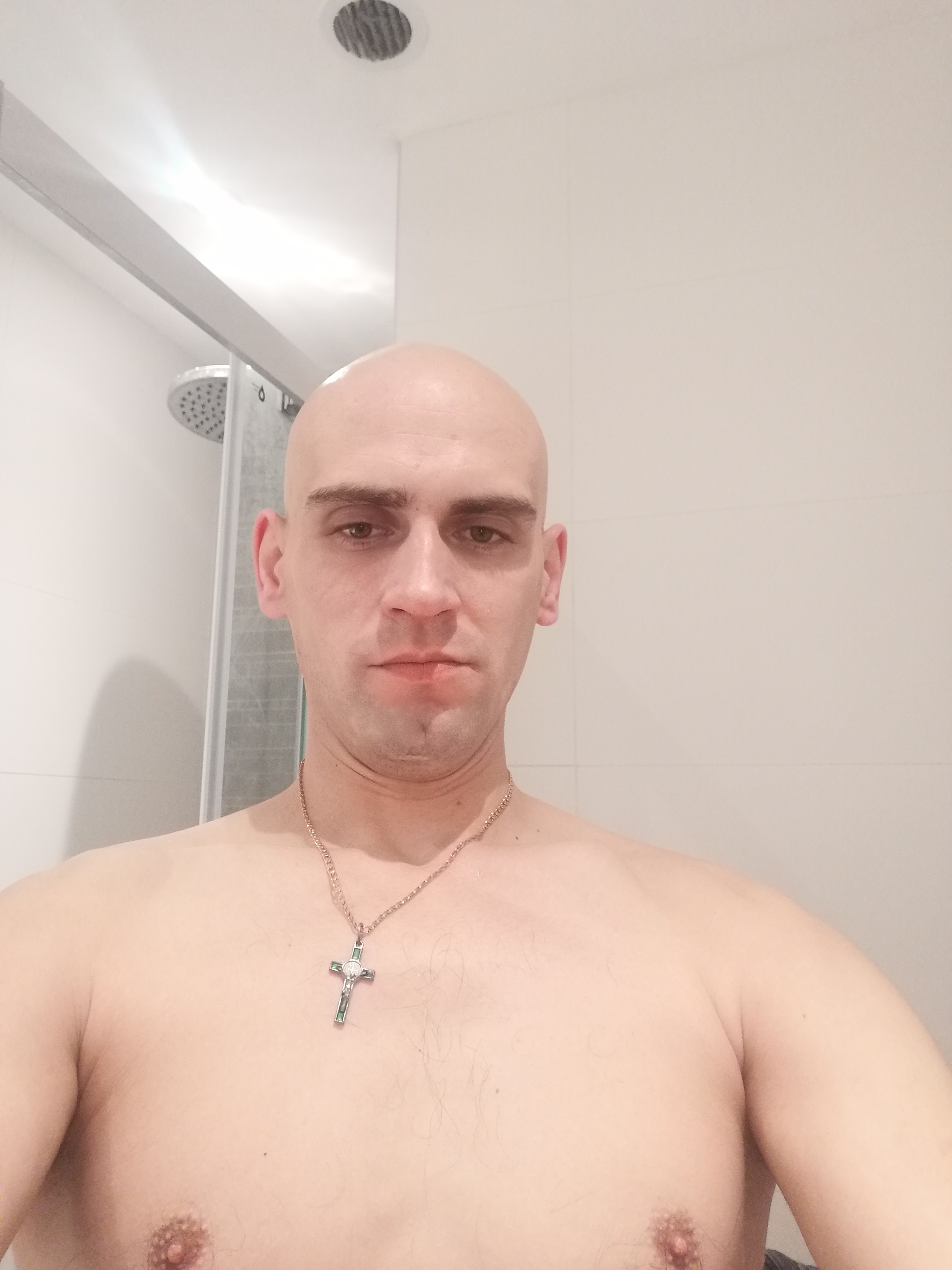 Portret łysiejącego mężczyzny w łazience w Bydgoszczy, na szyi złoty łańcuszek z krzyżykiem, widoczna kabina prysznicowa.