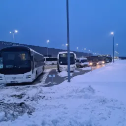 Rząd białych autobusów MAN zaparkowanych na ośnieżonym parkingu przed budynkiem Panattoni Europe o zmierzchu.