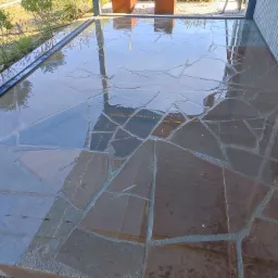 Świeżo ułożona, mokra posadzka z nieregularnych płyt kamiennych na tarasie, z widocznym systemem odprowadzania wody i odbiciem nieba.