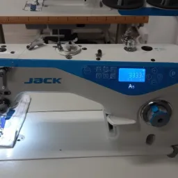 Nowoczesna, biało-niebieska maszyna do szycia marki Jack A5 z wyświetlaczem cyfrowym, przygotowana do pracy z niebieskim materiałem pod stopką.