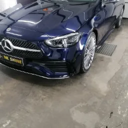 Błyszczący, granatowy Mercedes-Benz C-klasa po umyciu, z widocznym logo firmy detailingowej MK Shine na przednim zderzaku. W tle widoczna brama garażowa i kratka ściekowa w posadzce.
