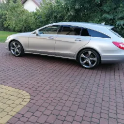 Srebrny Mercedes CLS Shooting Brake zaparkowany na podjeździe z kostki brukowej; widoczne przyciemnione tylne szyby.