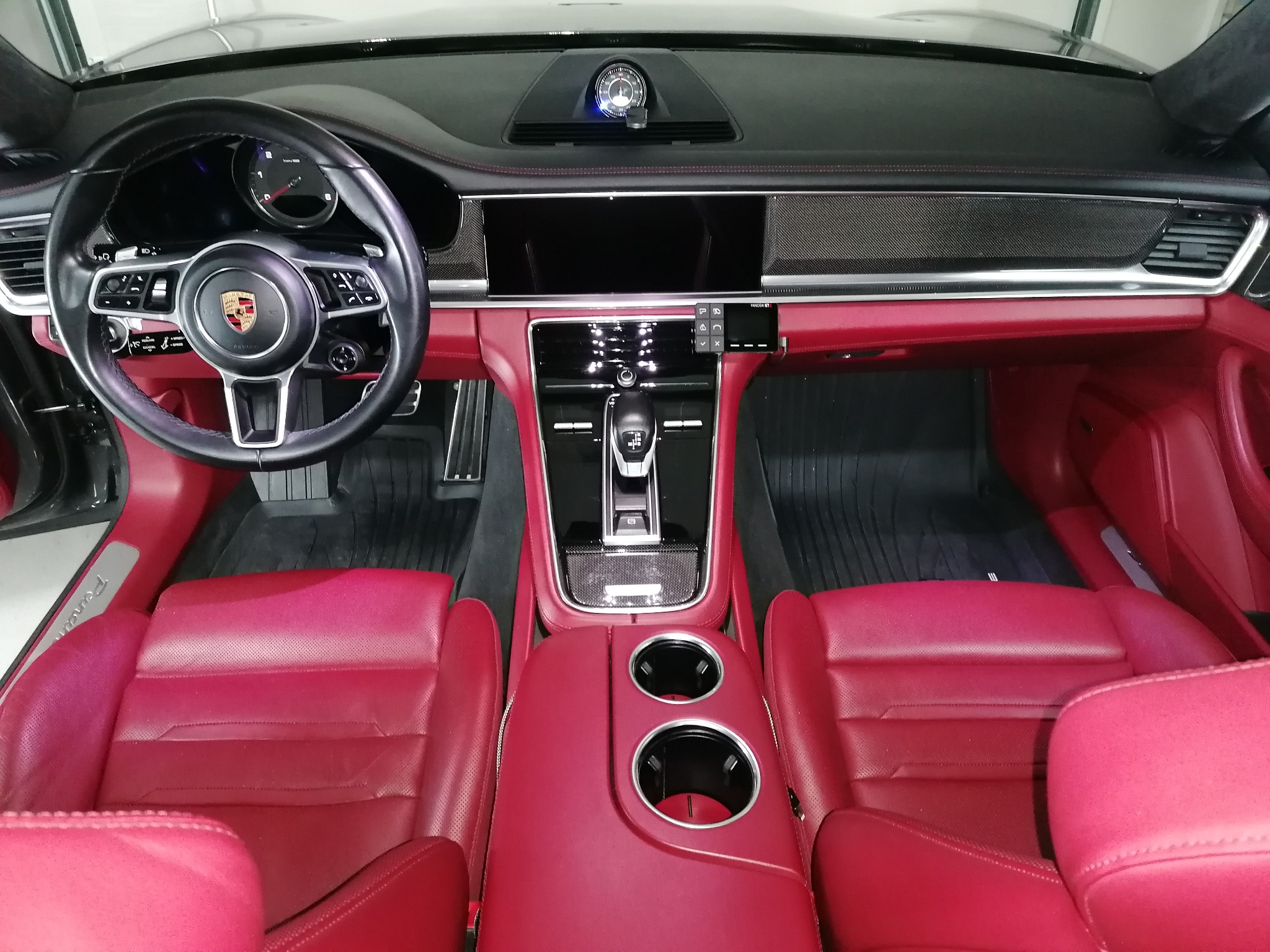 Wnętrze samochodu Porsche Panamera z czerwoną skórzaną tapicerką; widoczna deska rozdzielcza, kierownica z logo, fotele i konsola środkowa.