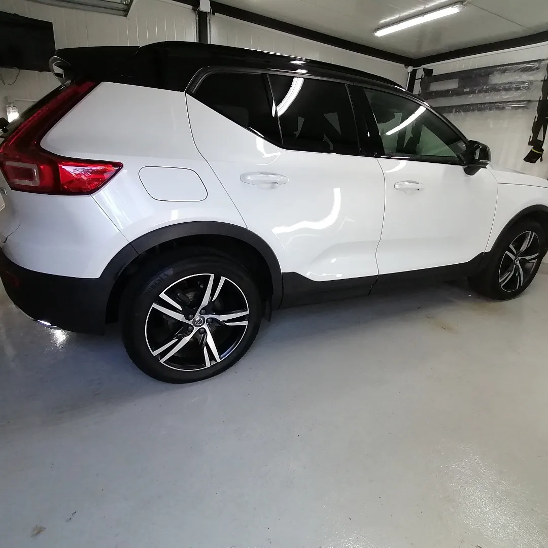 Biały samochód Volvo XC40 z przyciemnionymi szybami, zaparkowany w jasnym garażu, widok z boku.