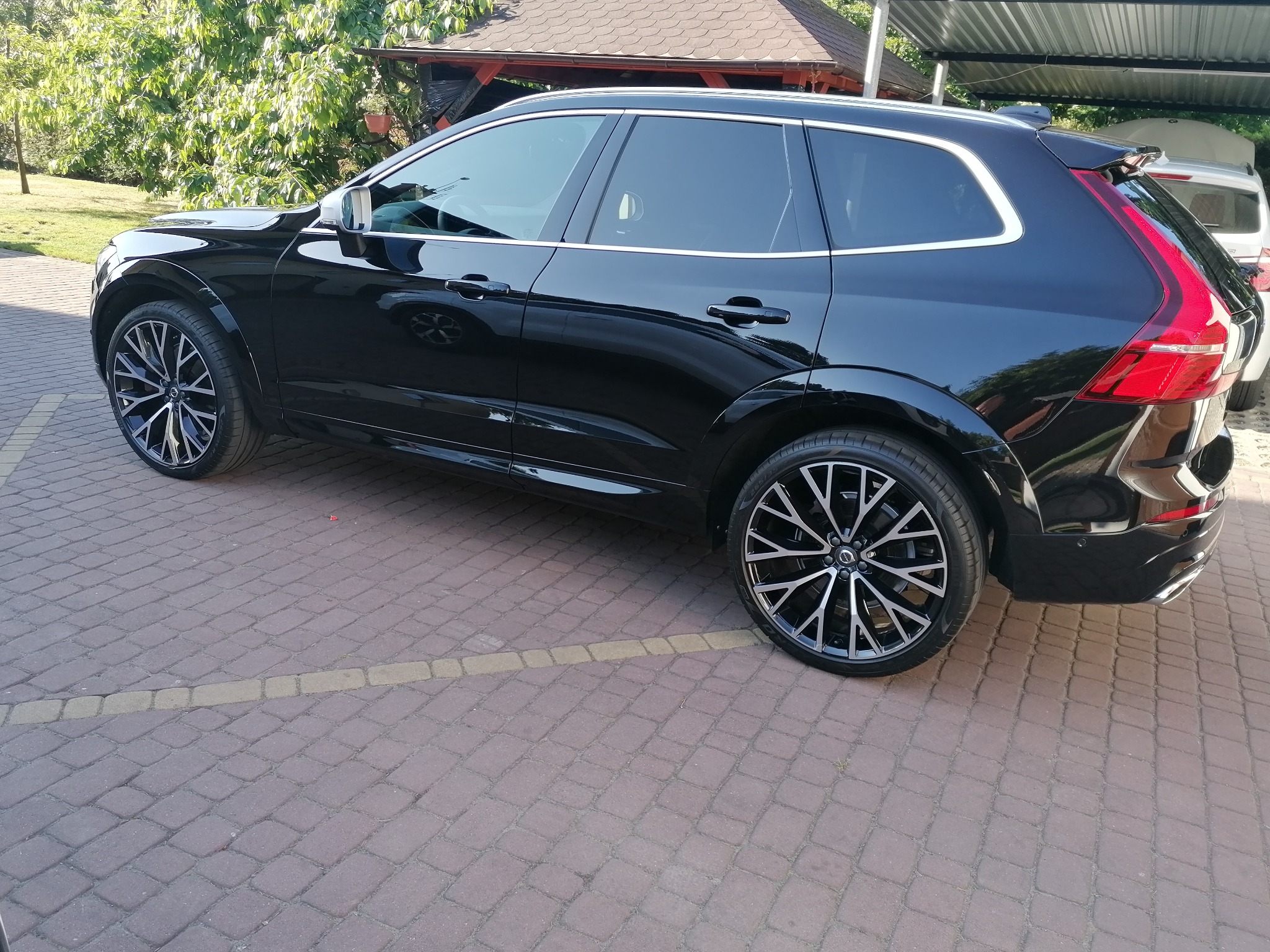 Czarny SUV Volvo z przyciemnionymi szybami bocznymi i tylną, zaparkowany na brukowanym podjeździe w słoneczny dzień.