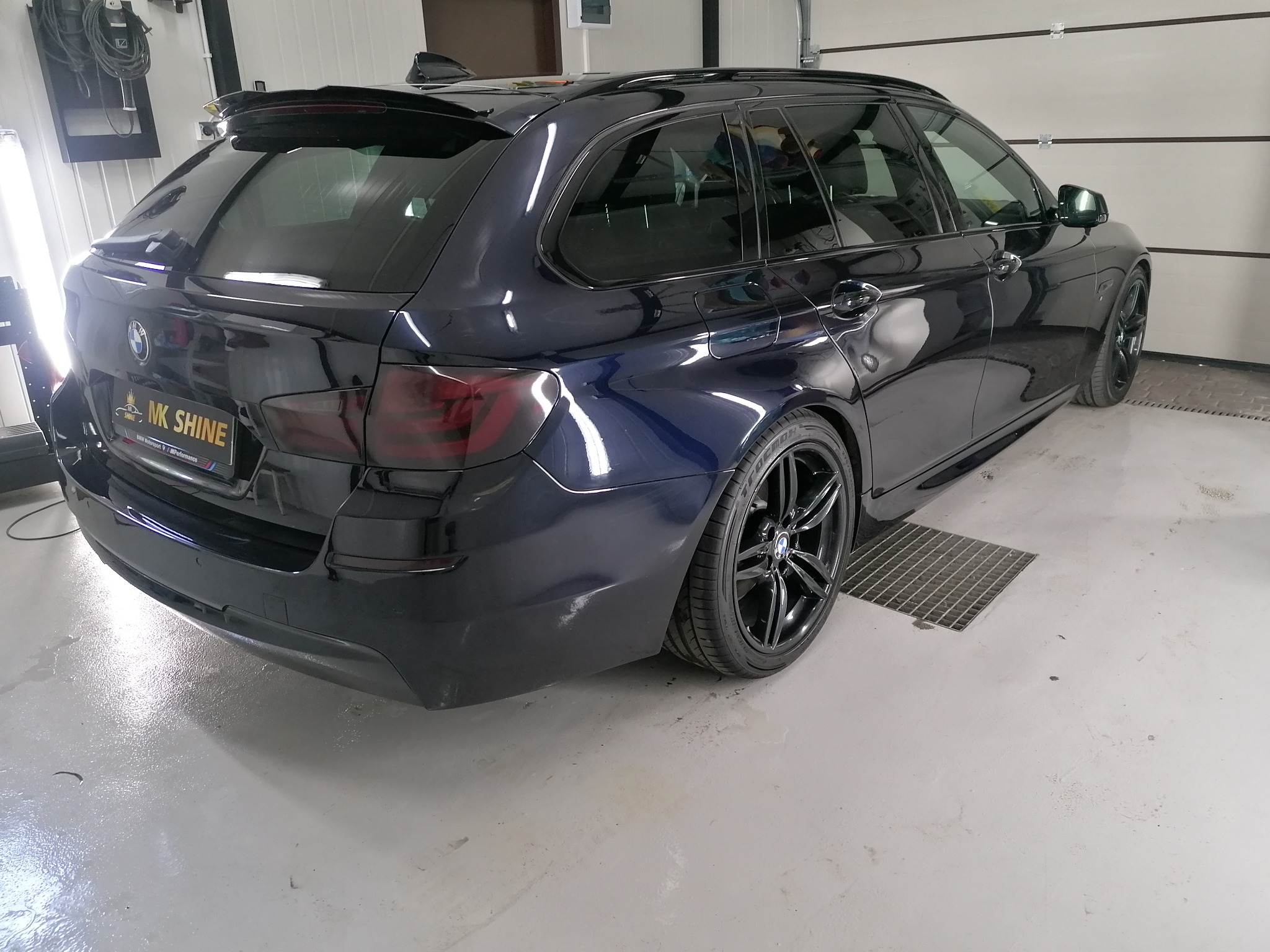 Granatowy samochód typu kombi marki BMW z przyciemnionymi tylnymi szybami i lampami, zaparkowany w sterylnym garażu z metalową kratką ściekową w podłodze.