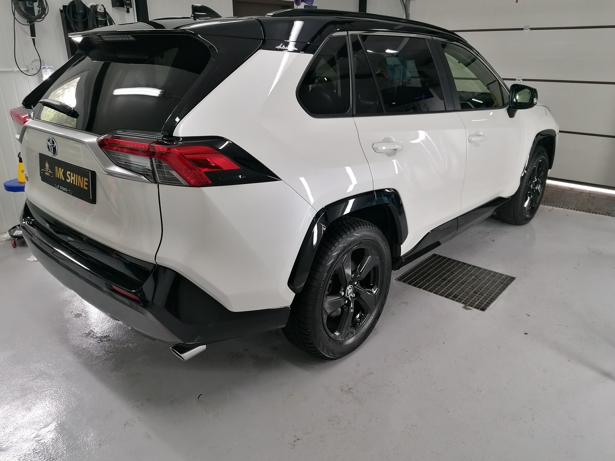 Biały samochód Toyota RAV4 z czarnymi akcentami po umyciu w myjni, widok z tyłu pod kątem, z widocznym logo firmy detailingowej.