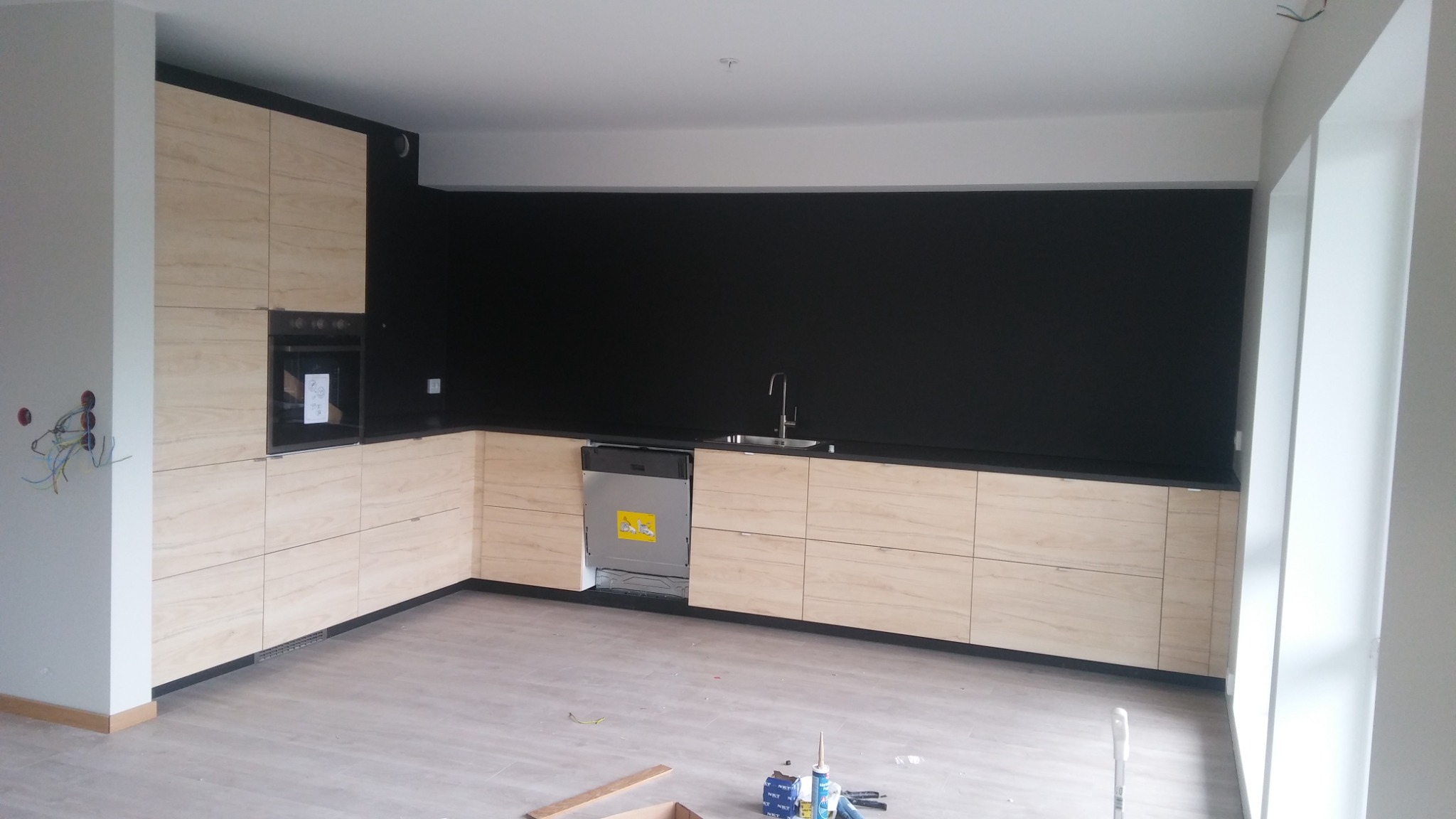 Nowoczesna kuchnia z drewnianymi szafkami i czarną ścianą w Szydłowcu, widoczne niedokończone prace wykończeniowe i narzędzia.