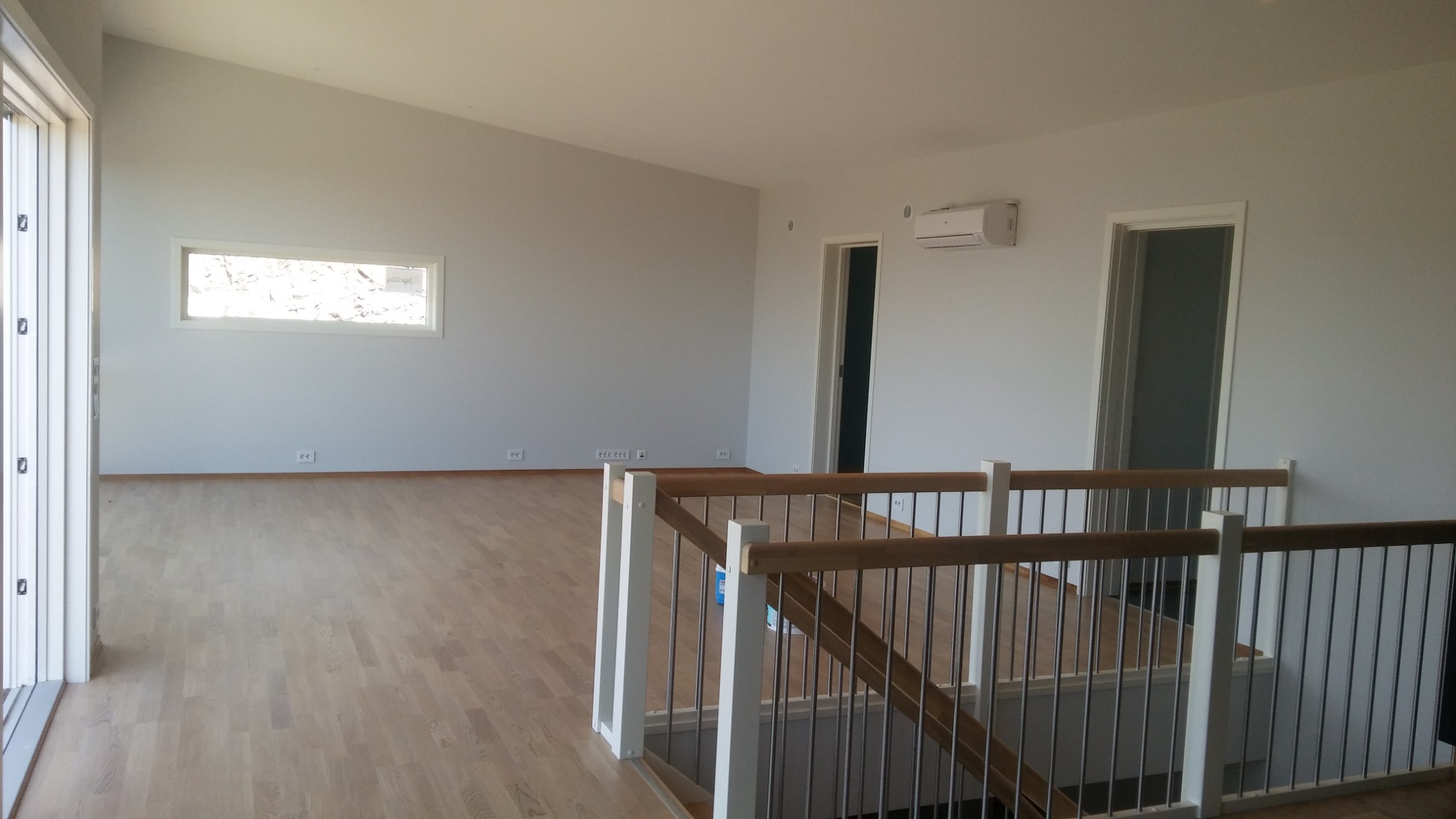 Jasne, przestronne wnętrze domu po remoncie, z drewnianą podłogą i świeżo wykończonymi ścianami w odcieniach bieli, widoczne schody z metalowymi i drewnianymi elementami oraz okno z widokiem...