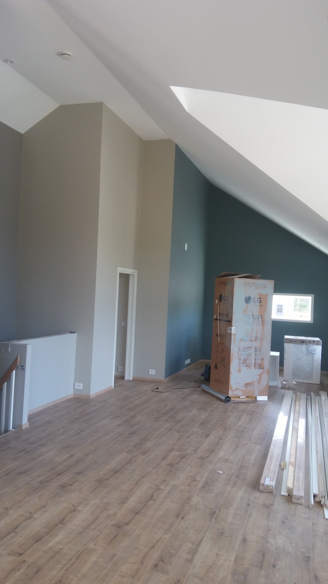 Wnętrze poddasza z pomalowanymi ścianami na szaro i granatowo, nowa podłoga, kartony po sprzęcie AGD i listwy przypodłogowe.