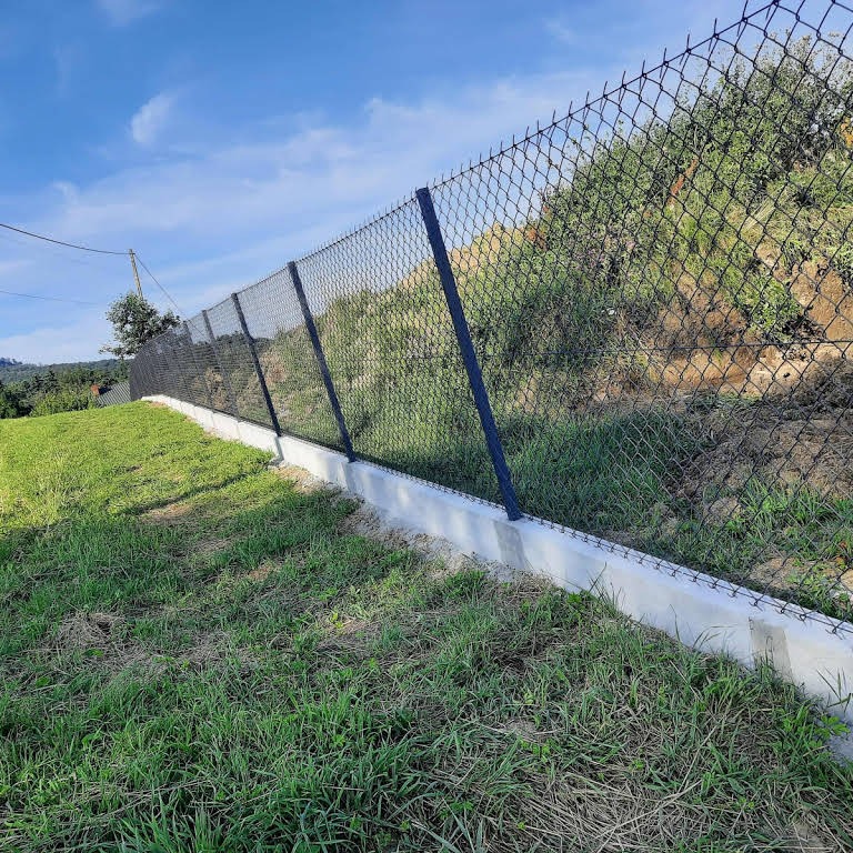 Ukończony montaż ogrodzenia z siatki na podmurówce betonowej, widok z dołu na zboczu, słupki w kolorze grafitowym.