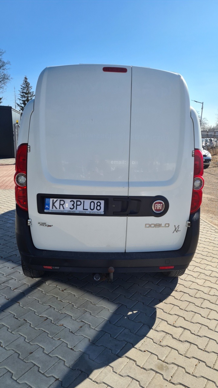 Tył białego samochodu dostawczego Fiat Doblo XL z tablicą rejestracyjną KR 3PL08, widoczny hak holowniczy.
