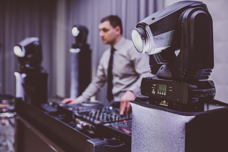 DJ obsługujący mikser z reflektorami scenicznymi na pierwszym planie, ustawienia oświetlenia na ekranie reflektora