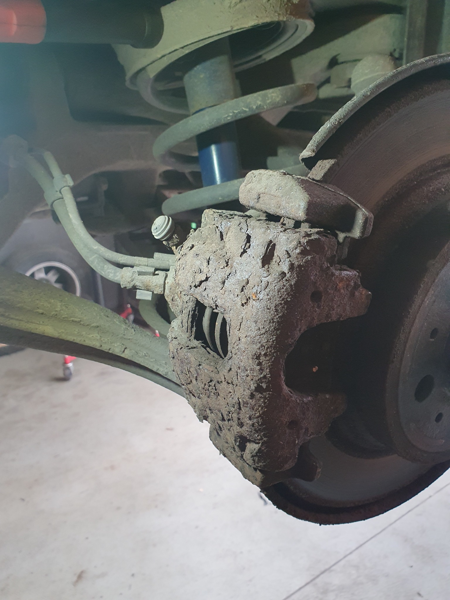 Silnie skorodowany zacisk hamulcowy z widoczną tarczą, sprężyną zawieszenia i elementami układu hamulcowego, wymagający wymiany lub renowacji.