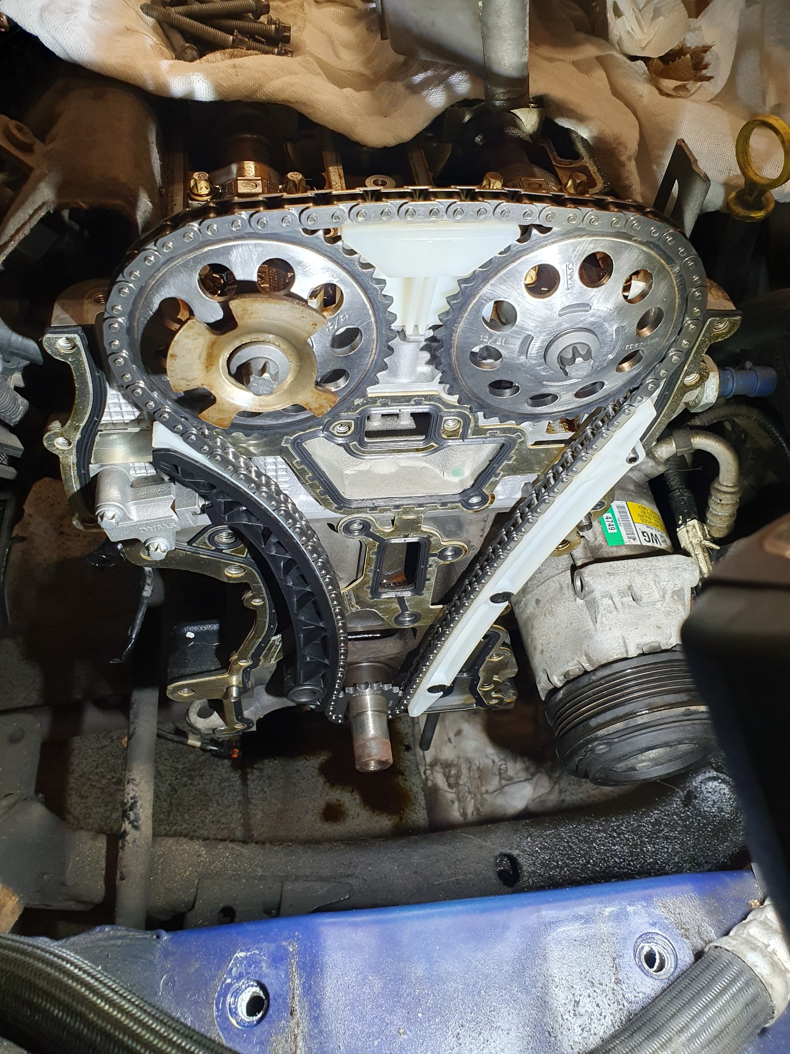 Silnik samochodowy z widocznym łańcuchem rozrządu, kołami zębatymi i elementami układu chłodzenia, w trakcie naprawy, z widocznymi śladami oleju.